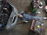 Механик в автосервисе ремонтирует автомобиль лежа на полу
